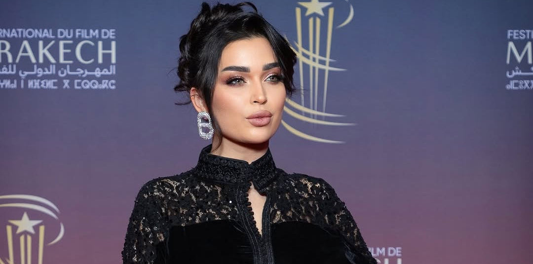 Woman in a black outfit posing against a promotional backdrop for the Marrakech International Film Festival.